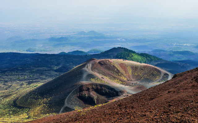 Blick auf Vulkankrater mit umliegender Landschaft und fernem Horizont.