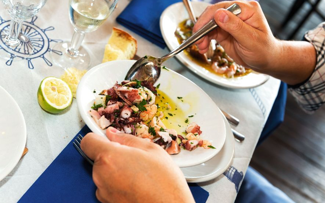 Teller mit Meeresfrüchtesalat, Brot, Zitronenscheibe und einem Glas Weißwein.