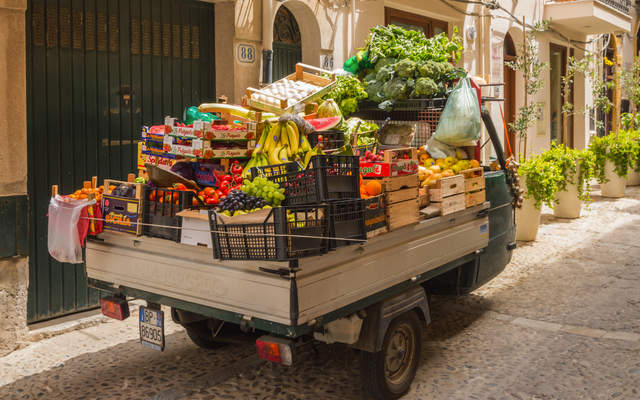 Kleiner Lkw mit Obst- und Gemüsekisten in einer engen Gasse geparkt.
