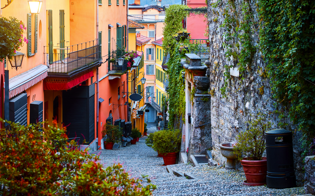 Gepflasterte Straße durch Bellagio am Comer See mit bunten Gebäuden und Pflanzen an den Fassaden.