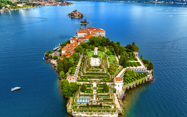 Luftaufnahme einer üppig begrünten Insel mit Gebäuden und geometrischen Gärten im See.