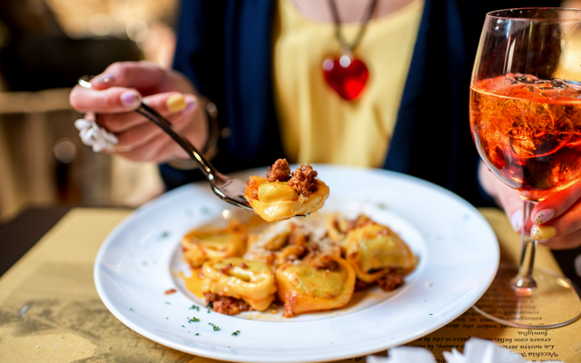 Person isst Pasta mit Fleischsauce, Glas Aperol Spritz daneben.