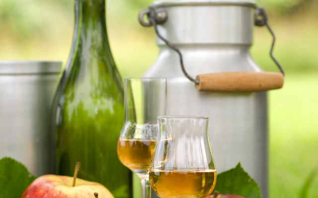 Äpfel, Schnapsgläser, Flasche und Milchkannen auf Holztisch im Freien.