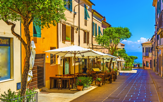 Straßencafé mit Sonnenschirmen in mediterranem Dorf.