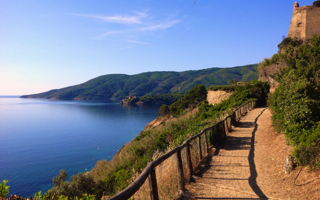 Küstenpfad mit Blick auf das Meer und Hügel im Hintergrund.