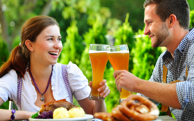 Ein Paar stößt mit Biergläsern an, draußen an einem Tisch sitzend.