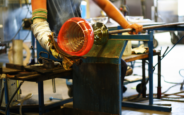 Person formt Glas mit Blasrohr in einer Werkstatt.