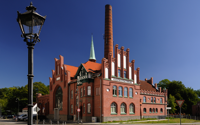 Rotes Backsteingebäude mit Turm, sonniger Tag, Laterne im Vordergrund
