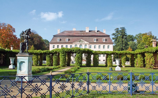Herrenhaus mit Garten und Statue im Vordergrund.