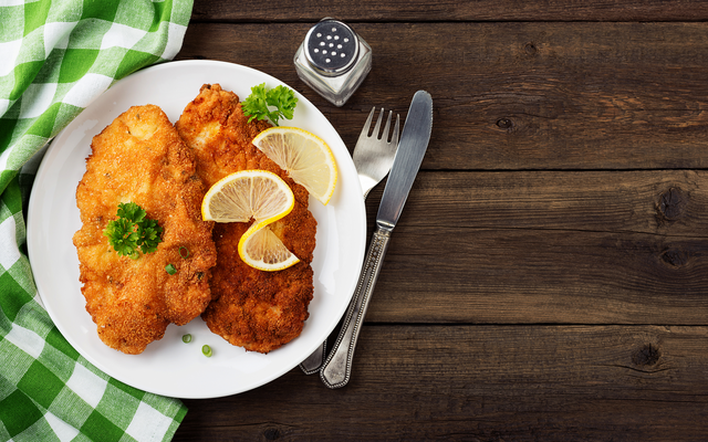 Zwei paniertes Schnitzel auf einem Teller mit Zitronenscheiben und Petersilie.