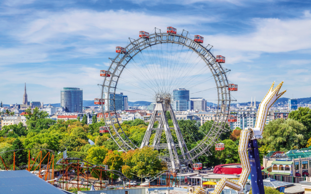 Riesenrad in einem Freizeitpark mit Stadtblick im Hintergrund an einem sonnigen Tag.