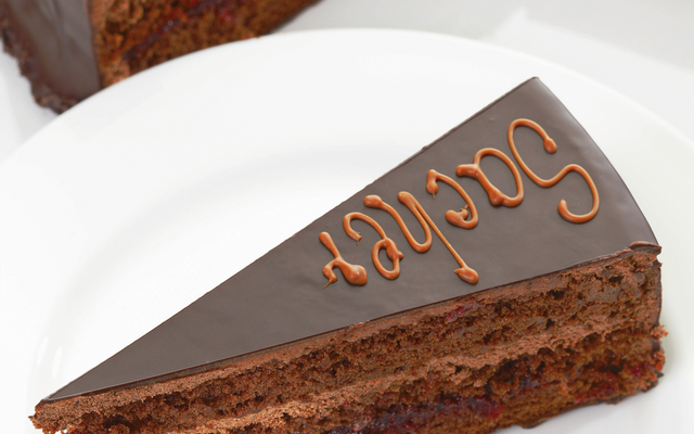 Ein Stück Schokoladenkuchen mit Glasur und Verzierung auf einem weißen Teller.