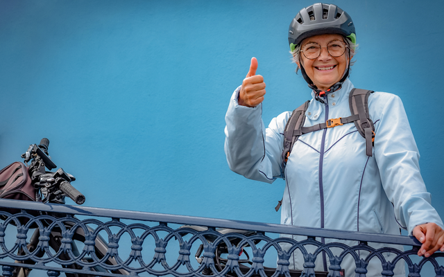 Person mit Fahrradhelm zeigt Daumen hoch neben Fahrrad.