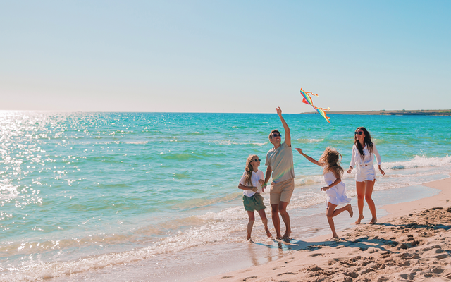 Familie fliegt einen Drachen am Strand bei sonnigem Wetter.