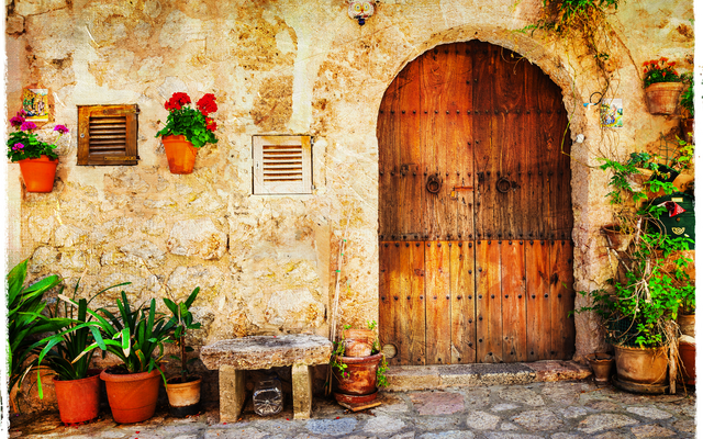 Steinarchitektur in Valldemossa, Mallorca, mit Holztür, umgeben von Topfpflanzen.