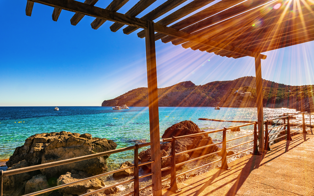 Promenade mit Blick auf das Meer, sonniger Himmel und Boote in der Ferne.