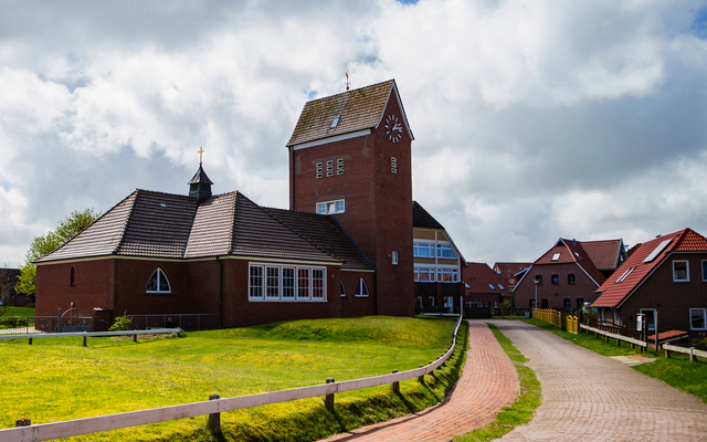 Backstein-Gebäude mit Uhrturm vor bewölktem Himmel und gepflastertem Weg.
