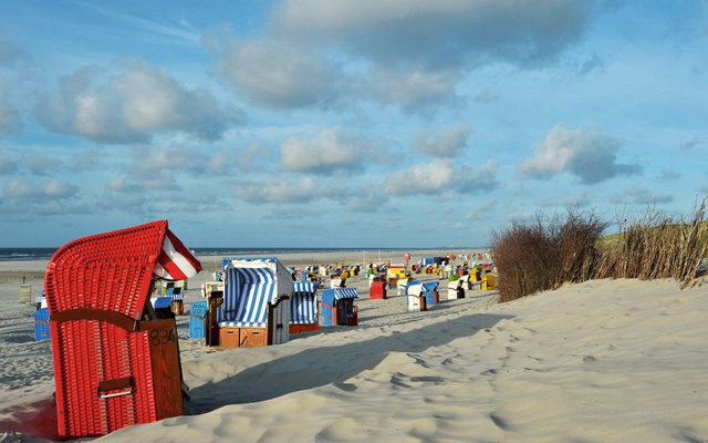 Strandkörbe auf einem sandigen Strand bei blauem Himmel und Wolken.
