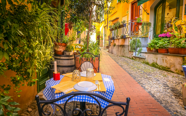 Gedeckter Tisch in einer malerischen Altstadtgasse mit Pflanzen und gelben Gebäuden.