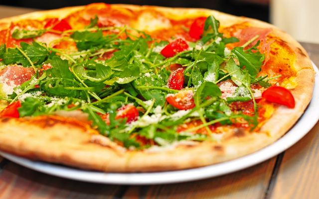 Pizza mit Rucola, Tomaten und Parmesankäse auf einem Holzuntergrund.
