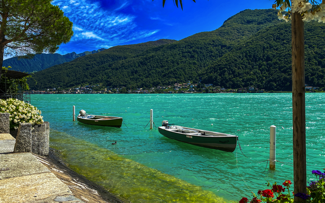 Zwei Boote auf einem türkisfarbenen See umgeben von Bergen und üppiger Vegetation.