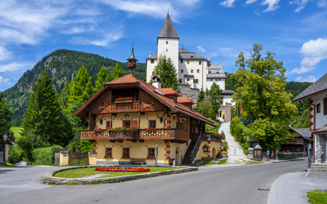 Idyllisches Bergdorf mit traditionellen Häusern und Burg im Hintergrund.