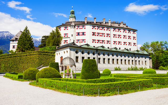 Schloss inmitten gepflegter Gärten und Hecken, blauer Himmel im Hintergrund.