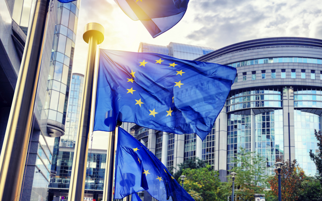 EU-Flaggen wehen vor einem modernen Gebäude in der Sonne.
