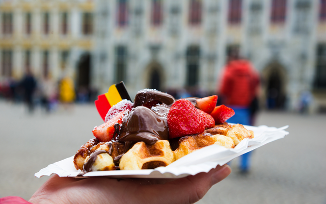Person hält Waffel mit Erdbeeren und Schokolade auf einem Teller.