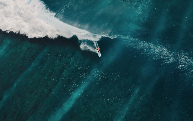 Surfer reitet auf großer Welle im klaren blauen Meer, Luftaufnahme.