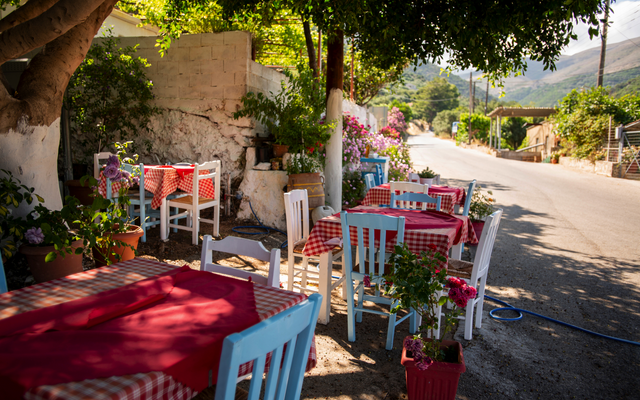 Bunte Stühle und Tische mit Tischdecken in einem sonnigen Straßencafé.