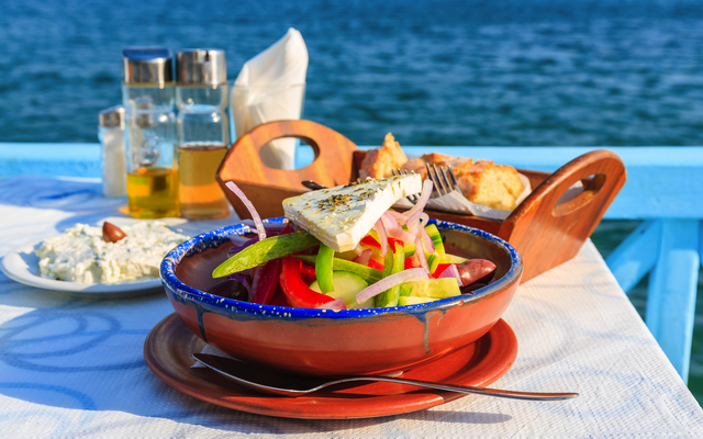 Griechischer Salat mit Meerblick im Hintergrund auf einem Tisch serviert.