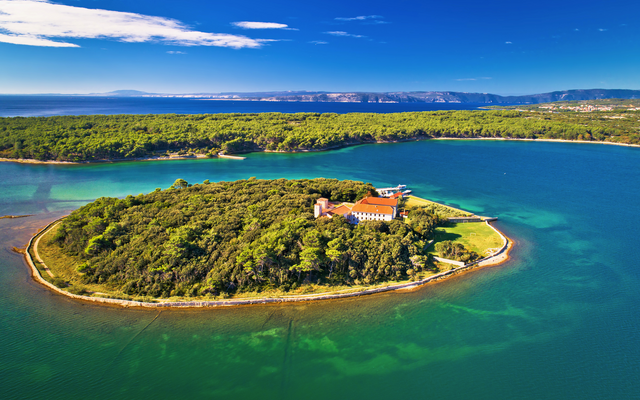 Kleine bewaldete Insel mit Gebäude, umgeben von türkisfarbenem Wasser.