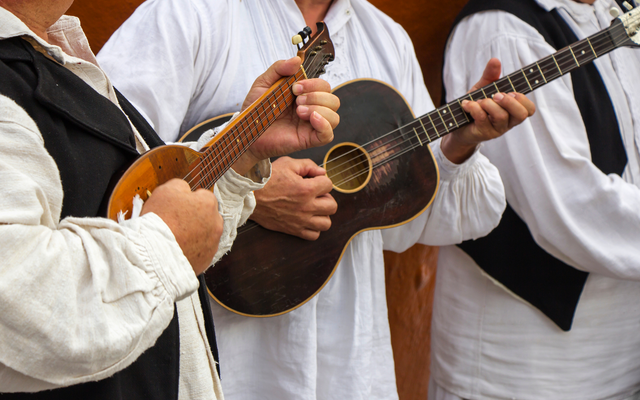Drei Musiker in traditioneller Kleidung spielen Gitarren und Mandoline.