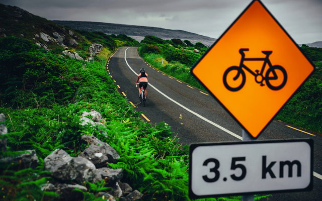 Radfahrer auf Straße mit Fahrradweg-Schild und 3,5 km Entfernungsangabe.