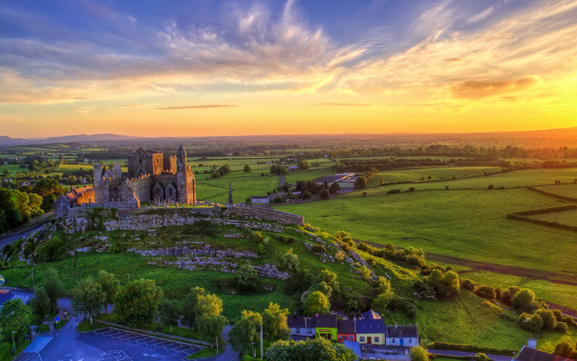 Burg auf Hügel in grüner Landschaft bei Sonnenuntergang.