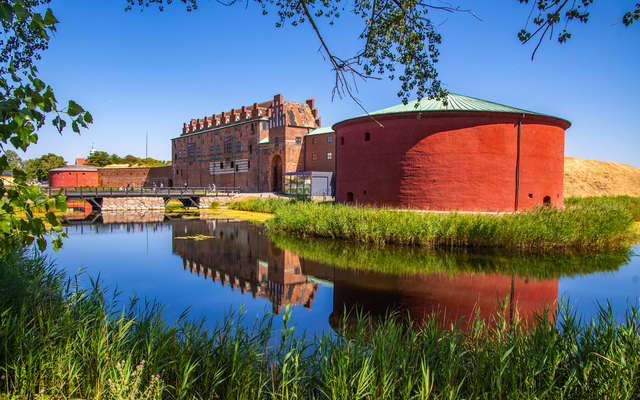 Schloss Malmöhus in Malmö, Schweden, bei klarem Wetter, umgeben von Wasser und Grünflächen.