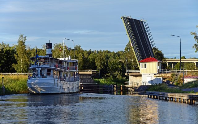 Ein Boot passiert eine geöffnete Zugbrücke an einem Fluss.