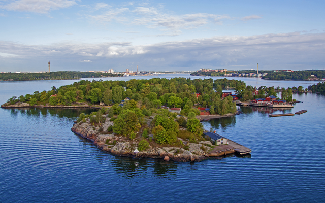 Kleine bewaldete Insel in einem großen Gewässer mit Häusern und Steg.