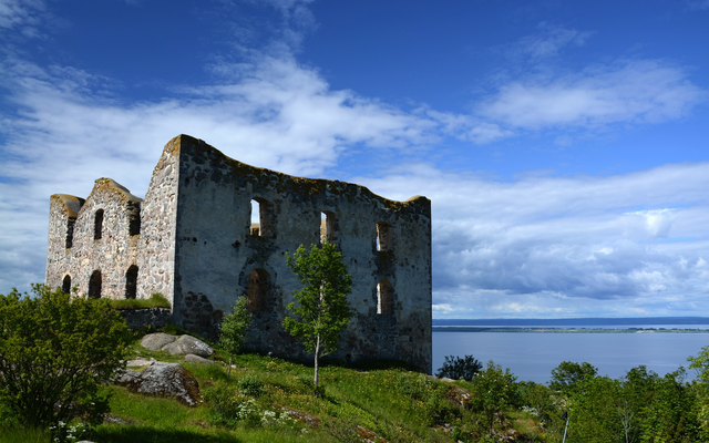 Ruine einer alten Steinburg vor einem See unter blauem Himmel.
