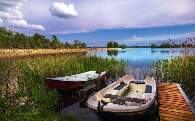 Zwei Boote an einem ruhigen See mit Gras und blauem Himmel im Hintergrund.