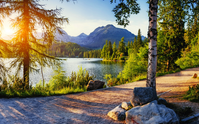 See mit Bäumen und Bergen im Hintergrund bei Sonnenschein