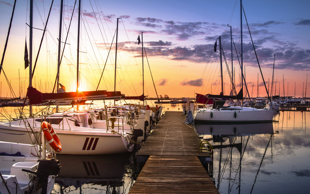 Yachthafen bei Sonnenuntergang mit Segelbooten am Steg.