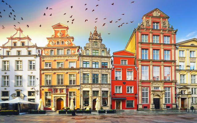 Historische Gebäude am zentralen Platz mit vorbeifliegenden Vögeln im Himmel.