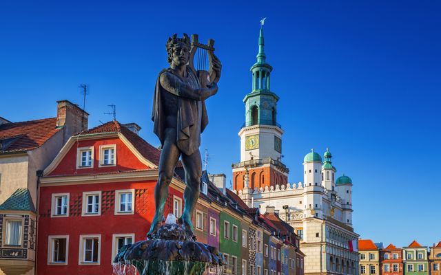 Statue eines Mannes mit Lyra vor bunten Gebäuden und einem Turm.