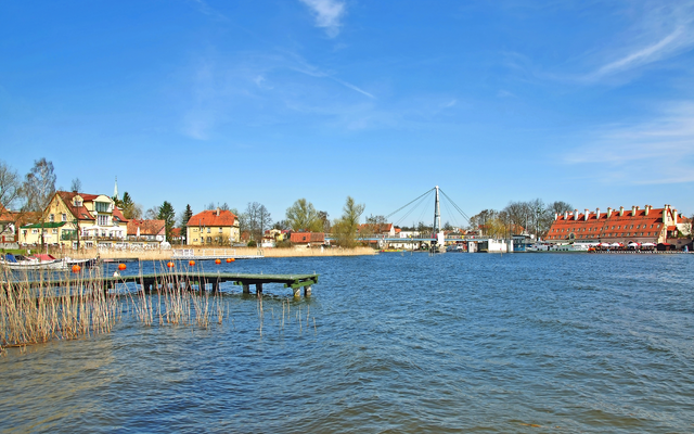 See mit Steg, Brücke und Stadt im Hintergrund bei klarem Himmel.