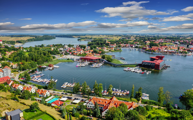 Stadtansicht mit Hafen, grüner Landschaft und Wasser an einem sonnigen Tag.