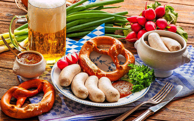 Bayerisches Frühstück mit Weißwürsten, Brezeln, Bier und Rettich auf Holztisch.