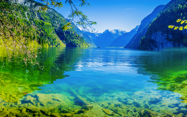 Bergsee mit klarem Wasser und umliegenden Bergen unter blauem Himmel.