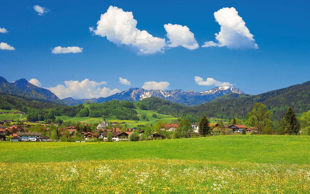 Landschaft in Inzell im Frühling mit Wiesen, Bergen und blauem Himmel.